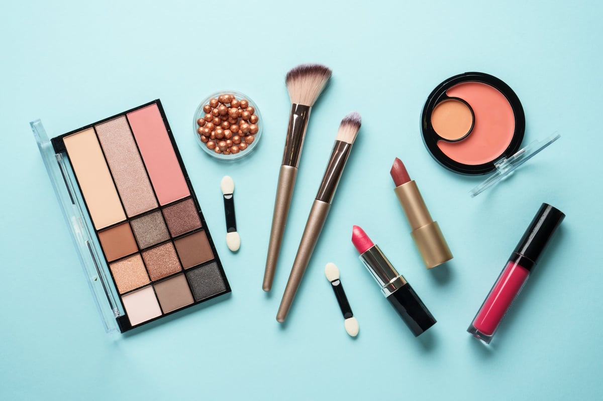 Makeup products on blue — cosmetic palette, brushes, lipsticks