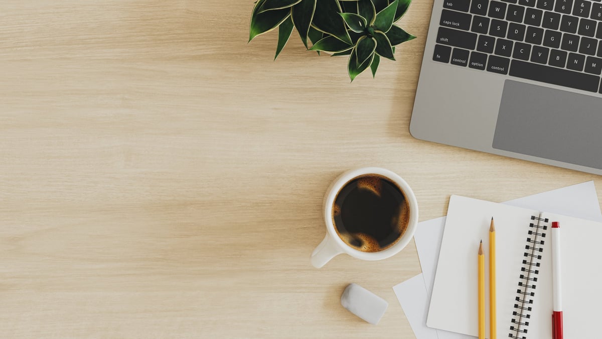 Wooden desk workspace flat lay with laptop, coffee, and plant